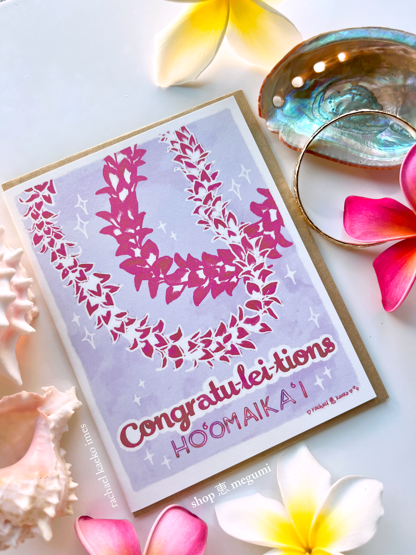 Hawaii-style greeting card that reads "Congratu-lei-tions" and "Ho'omaika'i" with floral design and text, surrounded by flowers and seashells on a light background.