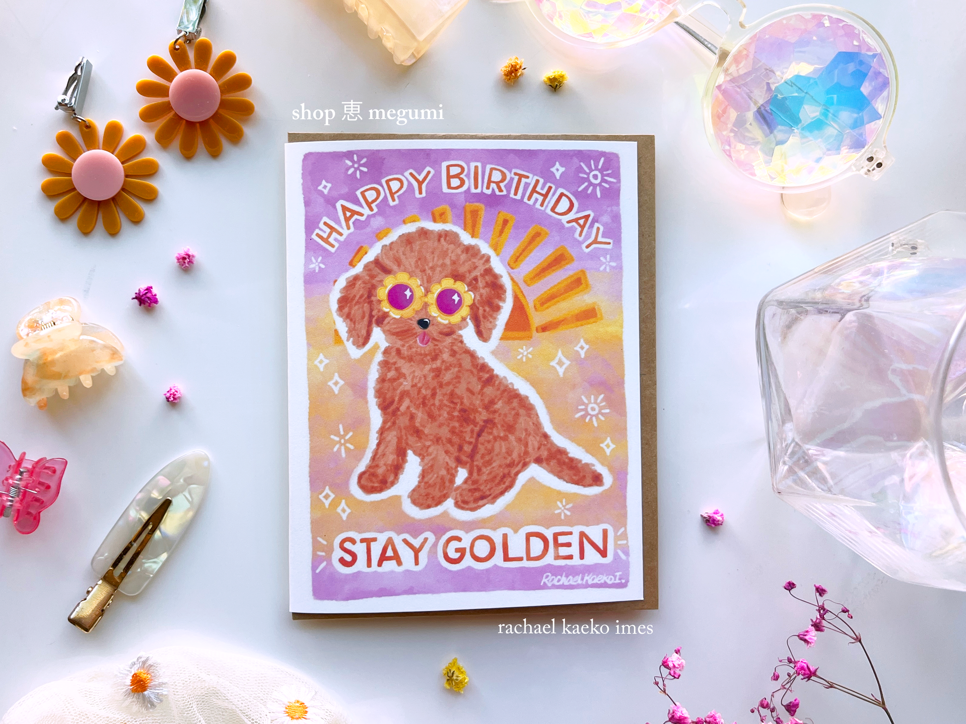 Birthday card with a cute golden doodle dog illustration and 'Happy Birthday Stay Golden' text with a sunset gradient background, on a decorative surface.