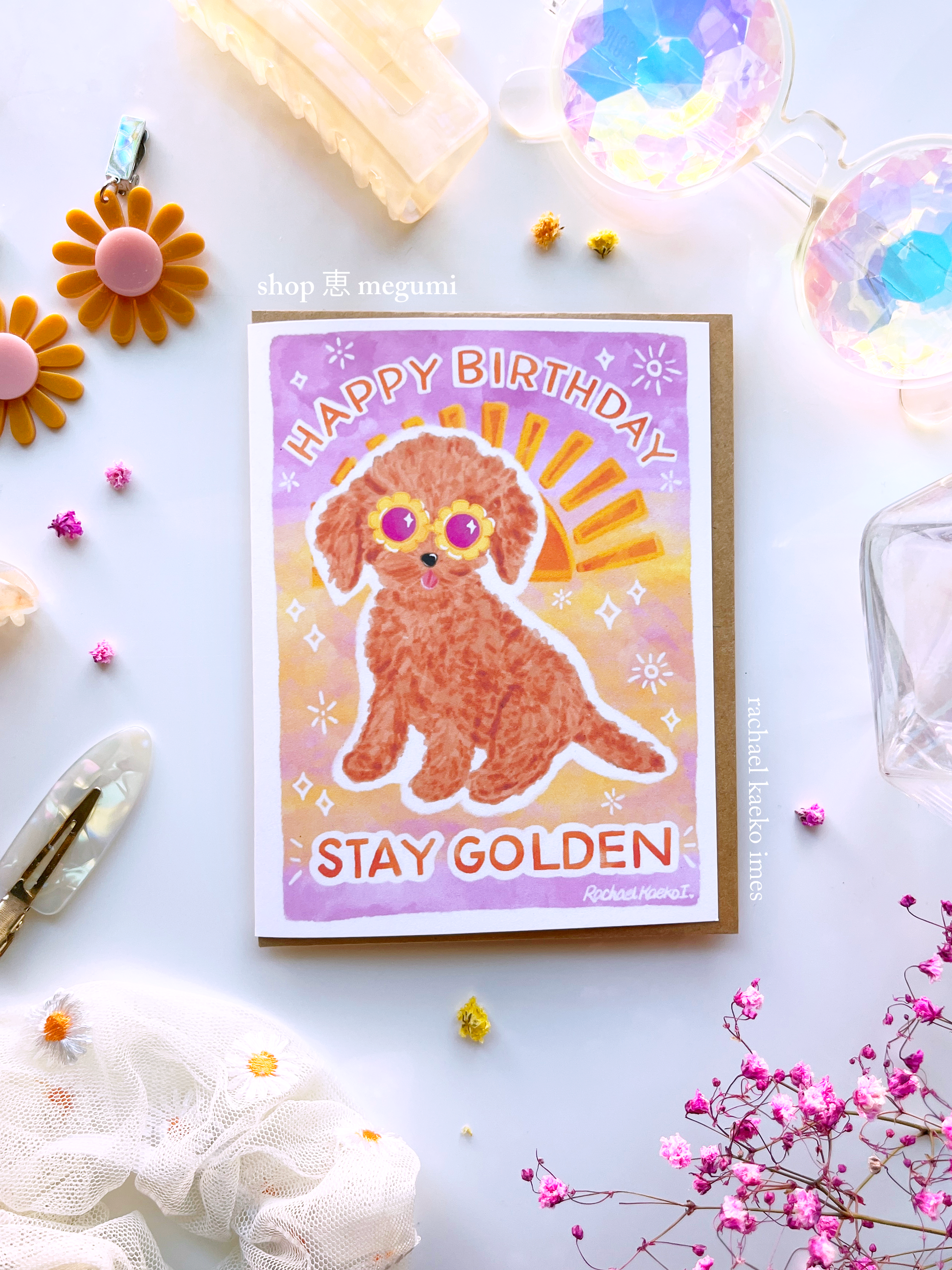 Birthday card with a cute golden doodle dog illustration and 'Happy Birthday Stay Golden' text with a sunset gradient background, on a decorative surface.