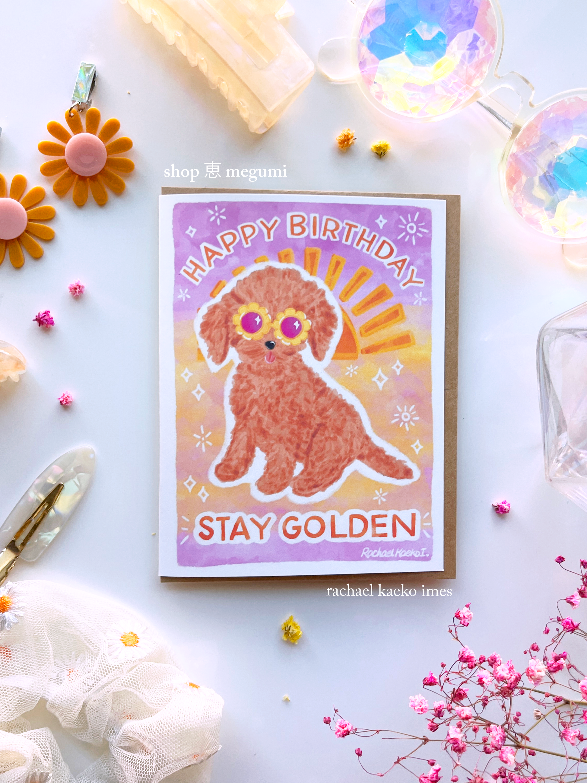 Birthday card with a cute golden doodle dog illustration and 'Happy Birthday Stay Golden' text with a sunset gradient background, on a decorative surface.