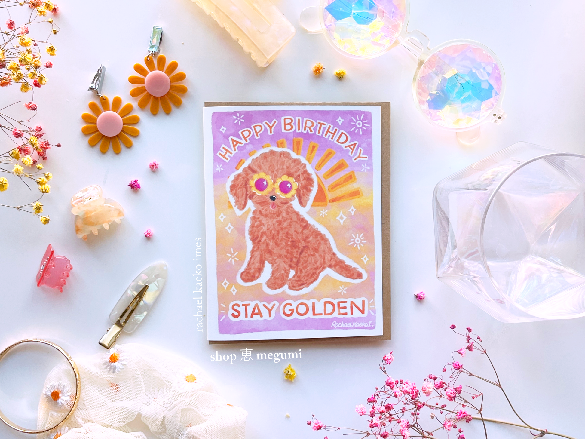 Birthday card with a cute golden doodle dog illustration and 'Happy Birthday Stay Golden' text with a sunset gradient background, on a decorative surface.