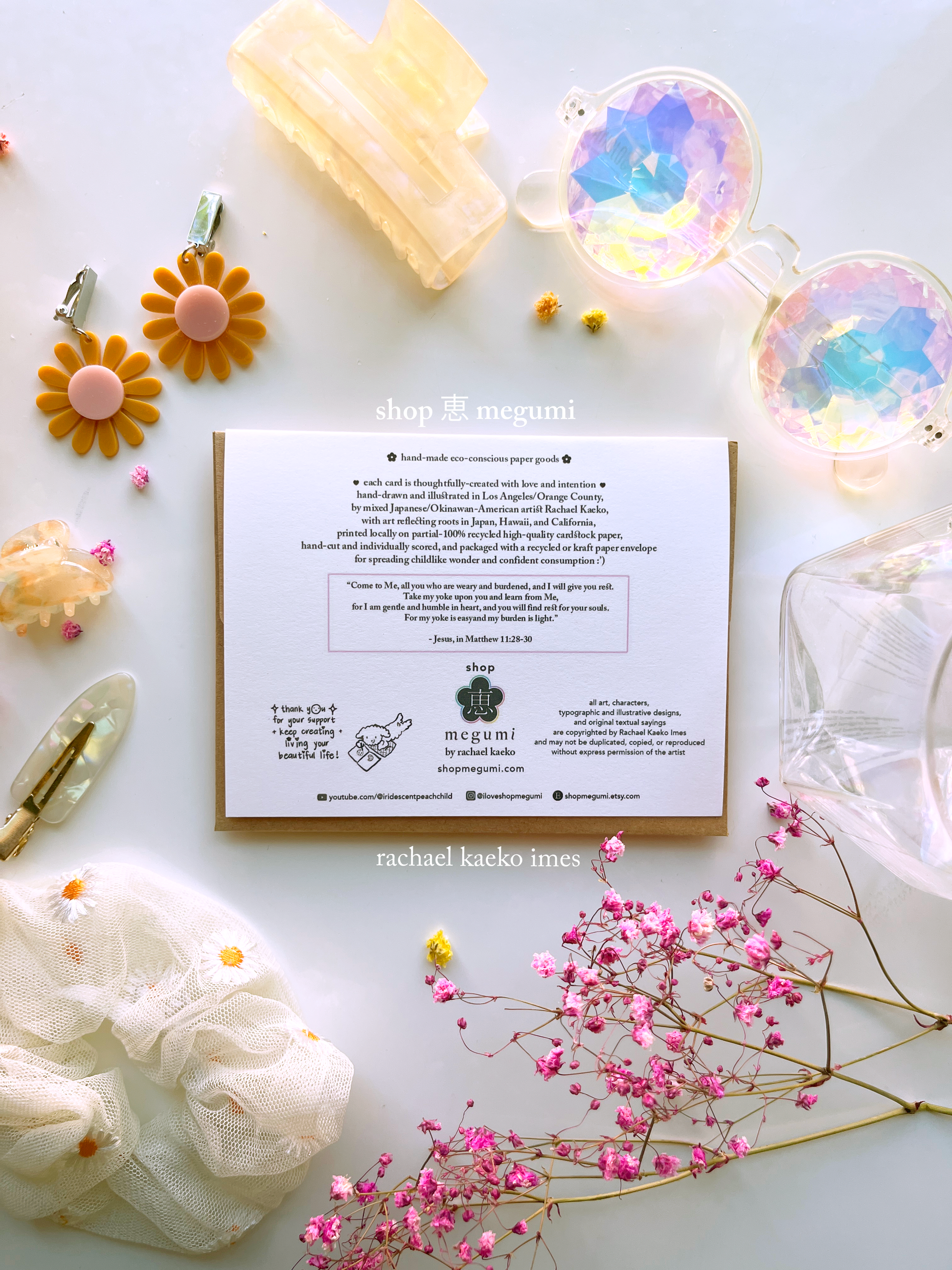 Back view of greeting card with product and branding information on a white surface, surrounded by colorful objects.