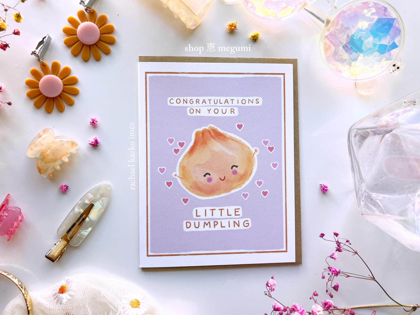 Greeting card with a cute illustration of a dumpling and text that reads "Congratulations on Your Little Dumpling" on a light background with decorative items.