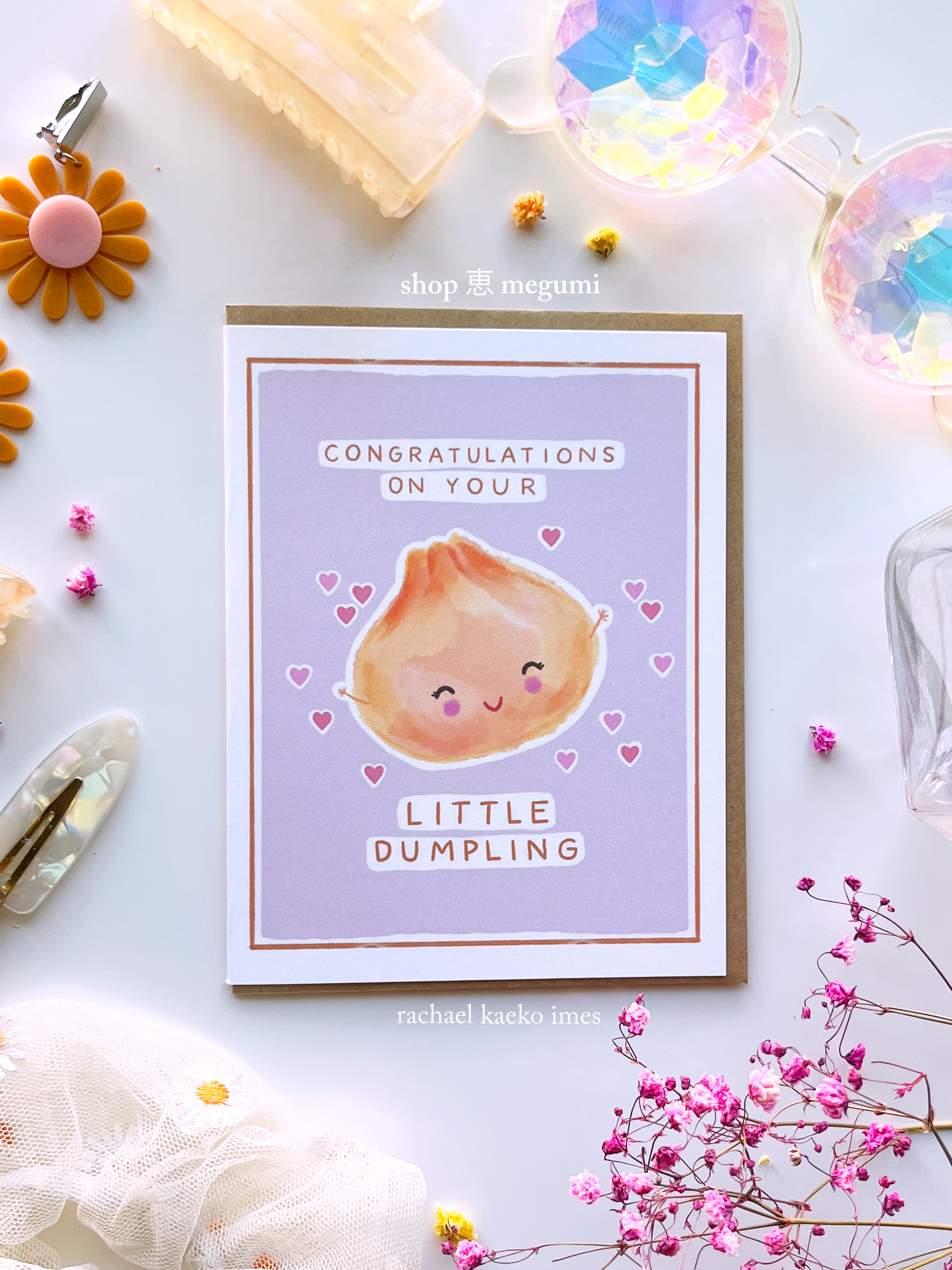 Greeting card with a cute illustration of a dumpling and text that reads "Congratulations on Your Little Dumpling" on a light background with decorative items.