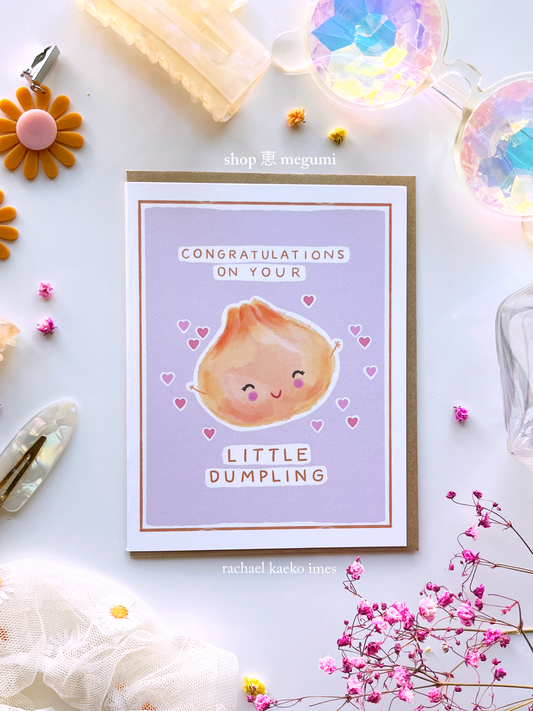 Greeting card with a cute illustration of a dumpling and text that reads "Congratulations on Your Little Dumpling" on a light background with decorative items.