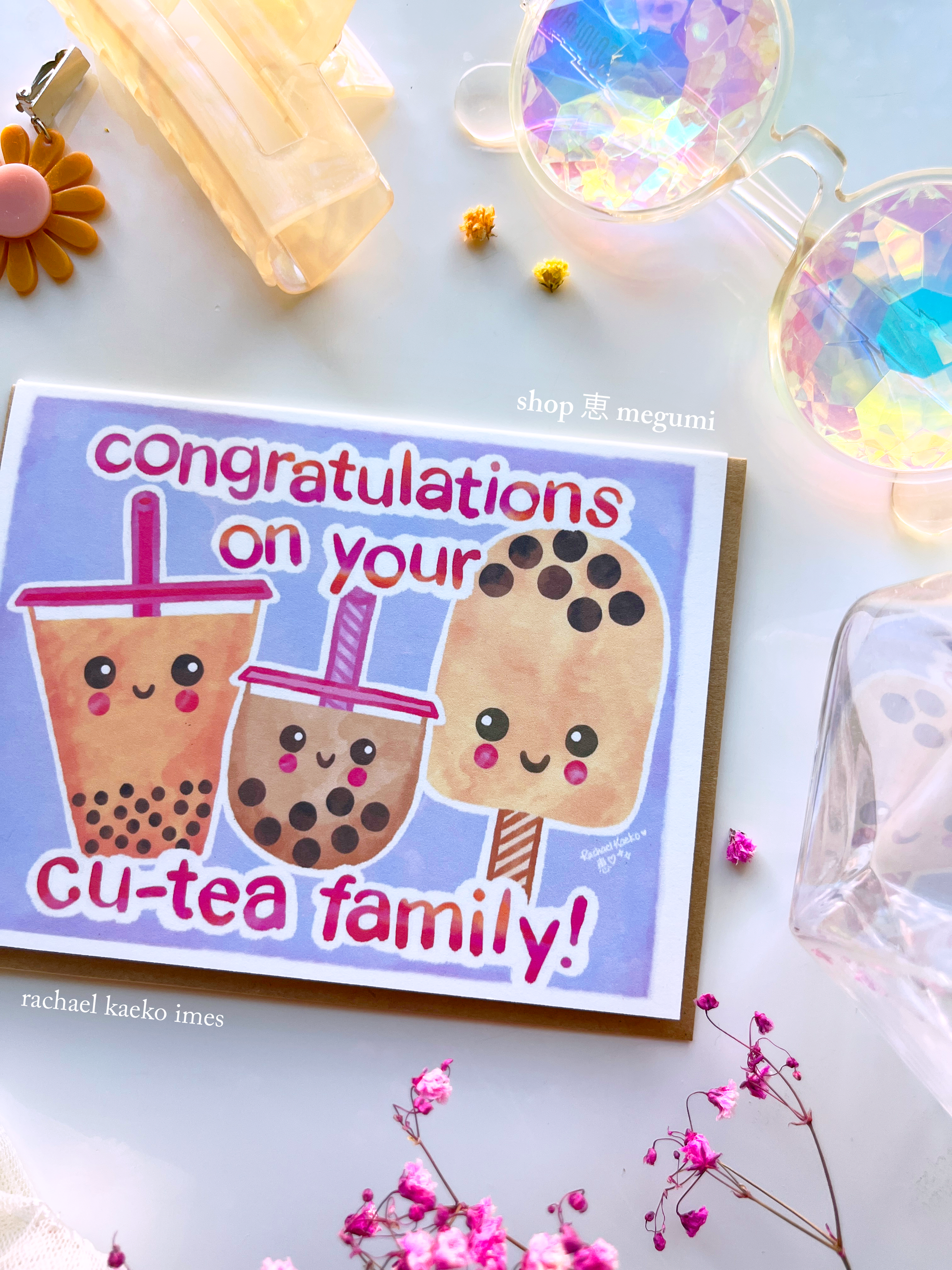 Close-up image of greeting card with illustrated bubble tea characters and text 'Congratulations on your cu-tea family!' on a light background.