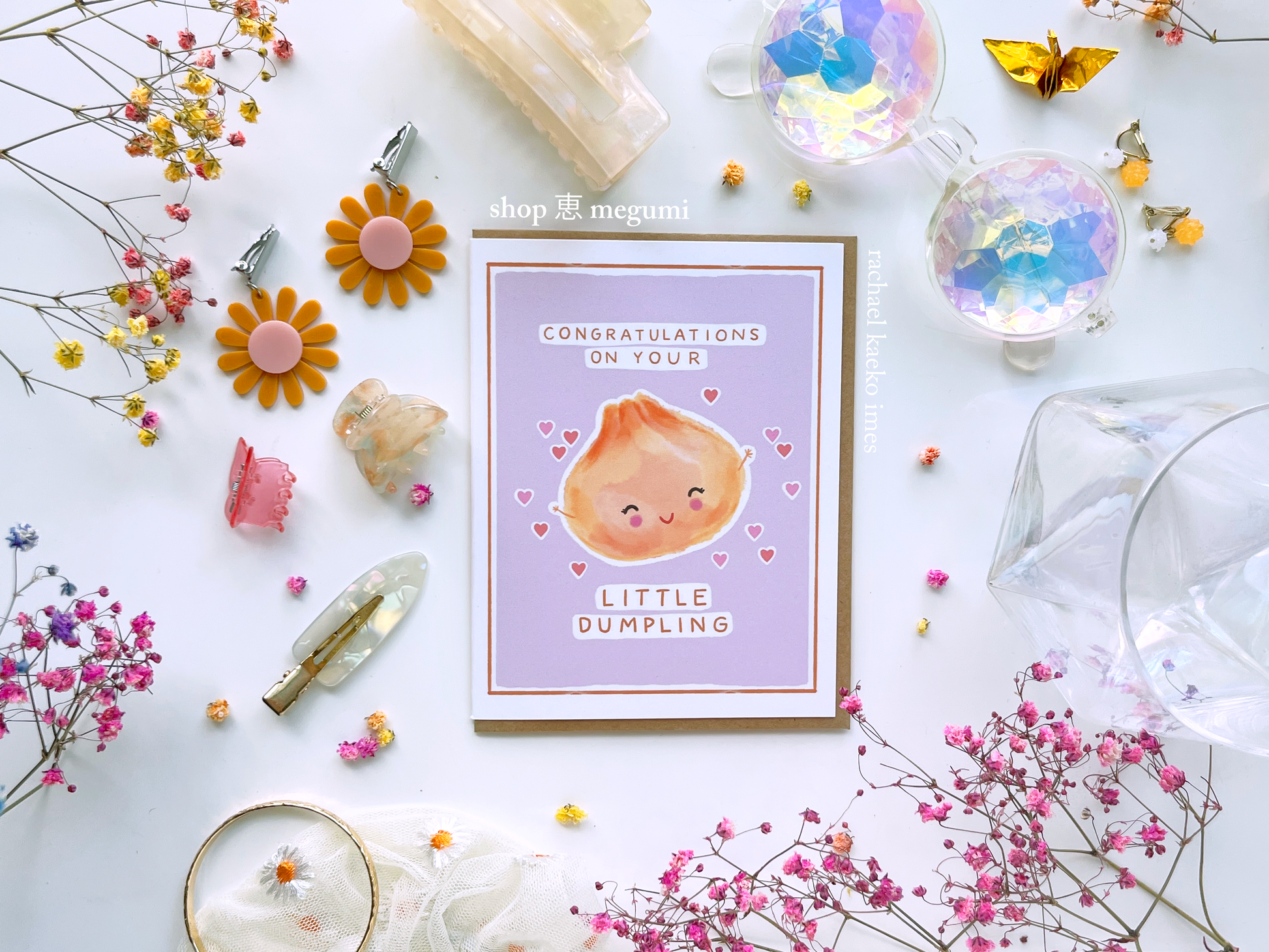 Greeting card with a cute illustration of a dumpling and text that reads "Congratulations on Your Little Dumpling" on a light background with decorative items.