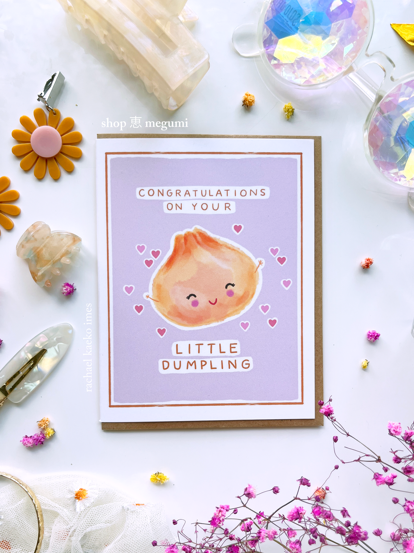 Greeting card with a cute illustration of a dumpling and text that reads "Congratulations on Your Little Dumpling" on a light background with decorative items.