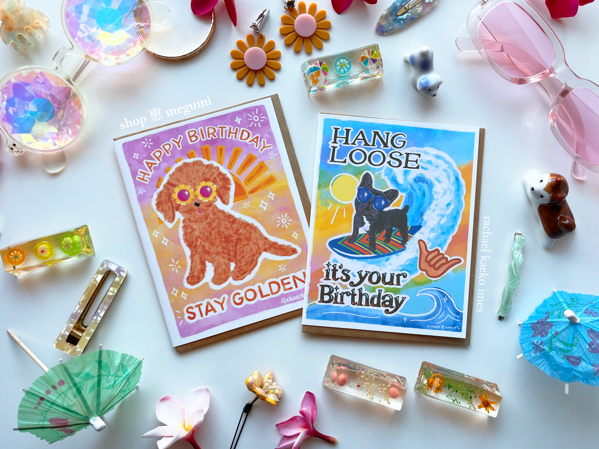 Two hand-drawn birthday cards with cute dogs wearing sunglasses surrounded by decorative items on a white surface.