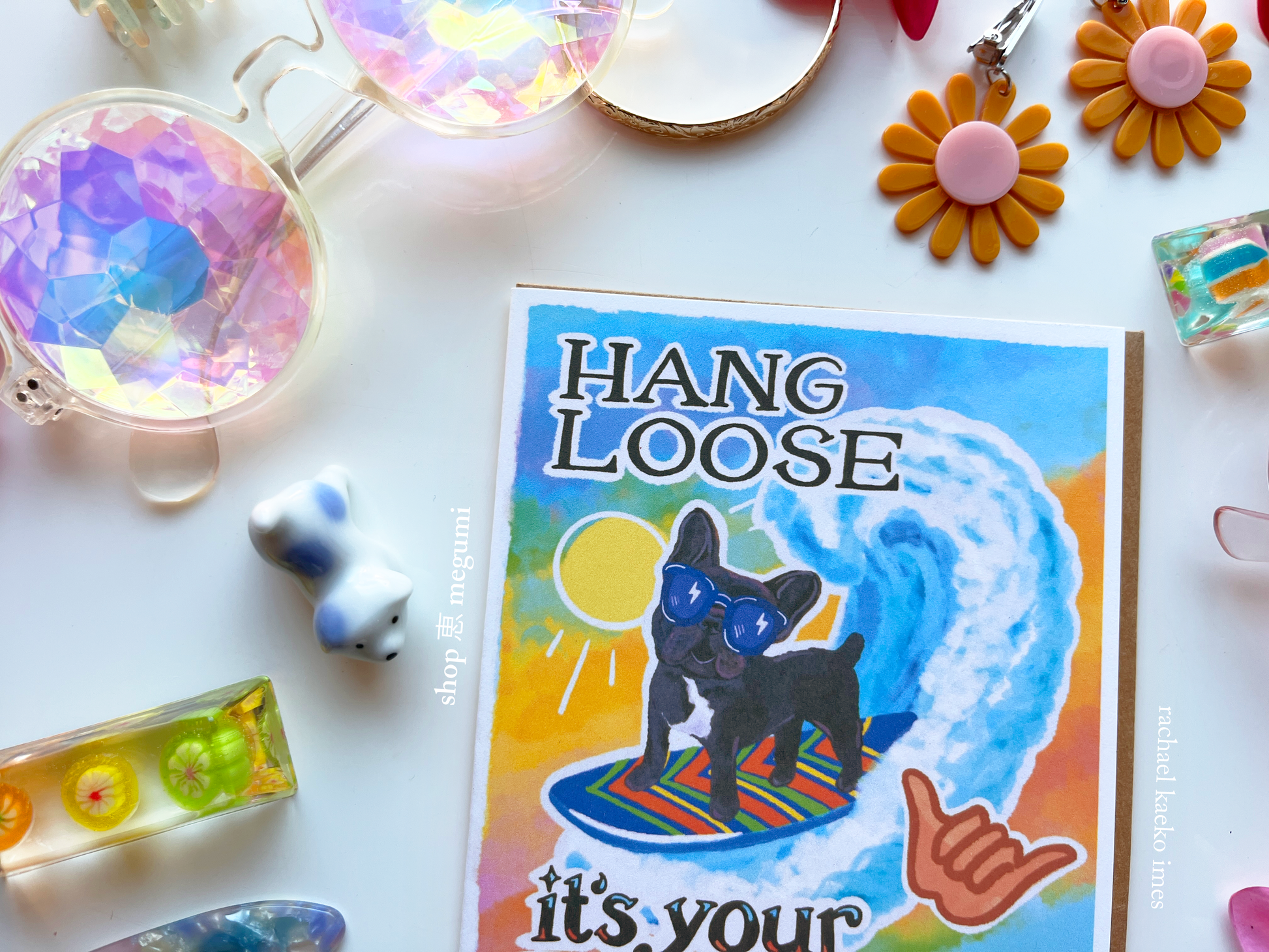Colorful card with a dog illustration and 'Hang Loose' text, surrounded by decorative items on a white surface.