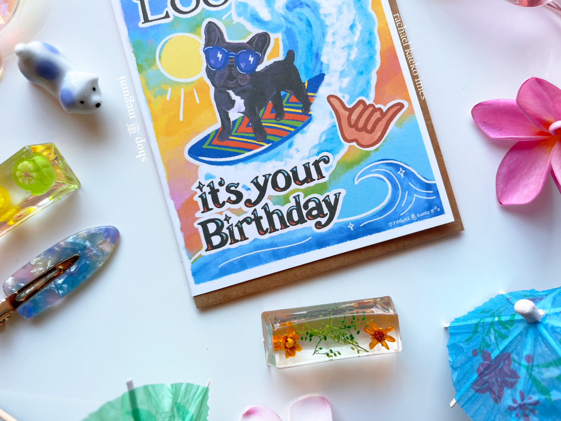 Cute french bulldog birthday card with a puppy surfing design surrounded by decorative items on a white surface