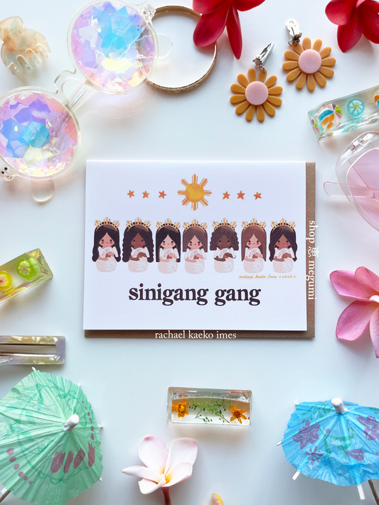 Cute hand-drawn greeting card with original copyrighted shop megumi megumi kin filipina kokeshi girls illustrations by Rachael Kaeko Imes, on a white surface with decorative items.