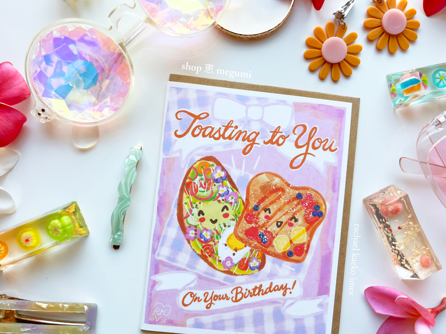 Close-up of cute coquette illustration of a french toast and avocado toast greeting card surrounded by decorative items on a white background