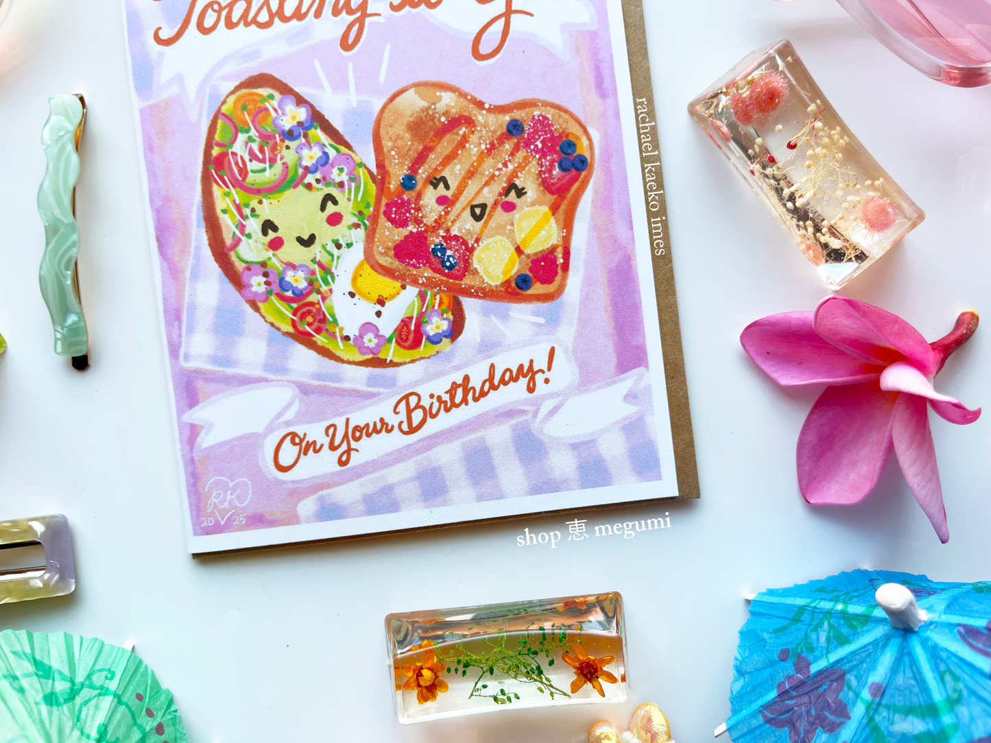 Close-up of cute birthday card with smiling breakfast foods surrounded by decorative items on a white surface.