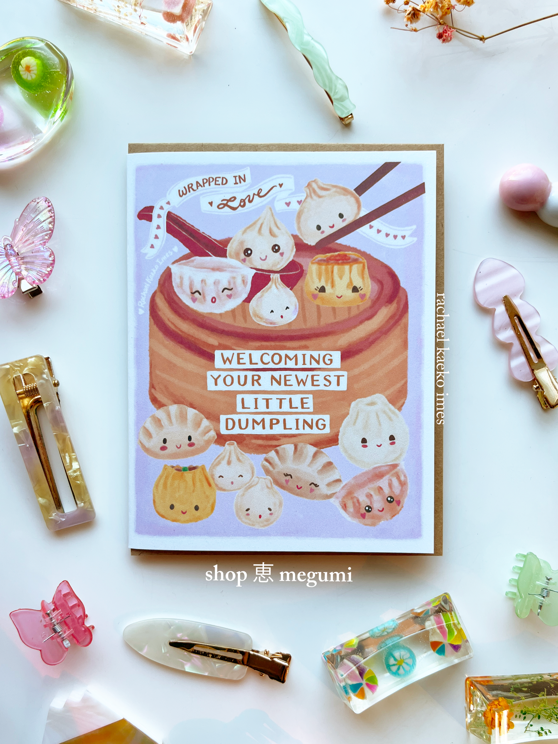 Kawaii baby shower card with cute dumpling illustrations and text on a white background with decorative items.