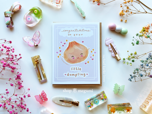 Cute baby shower card with a cute illustration of a dumpling surrounded by decorative items on a white background.