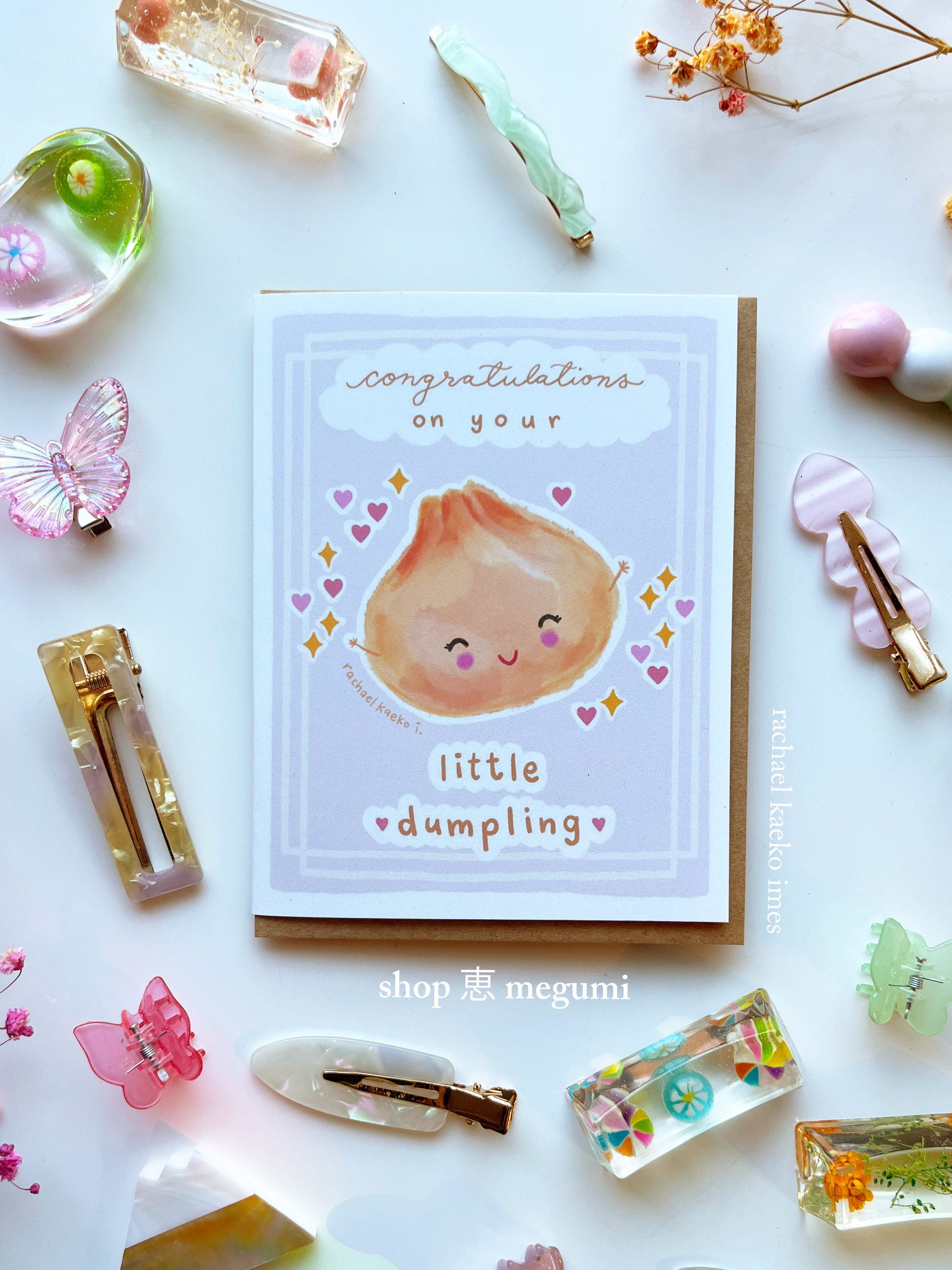 Kawaii baby greeting card with a cute illustration of a dumpling and text 'Congratulations on your Little Dumpling' surrounded by decorative items.