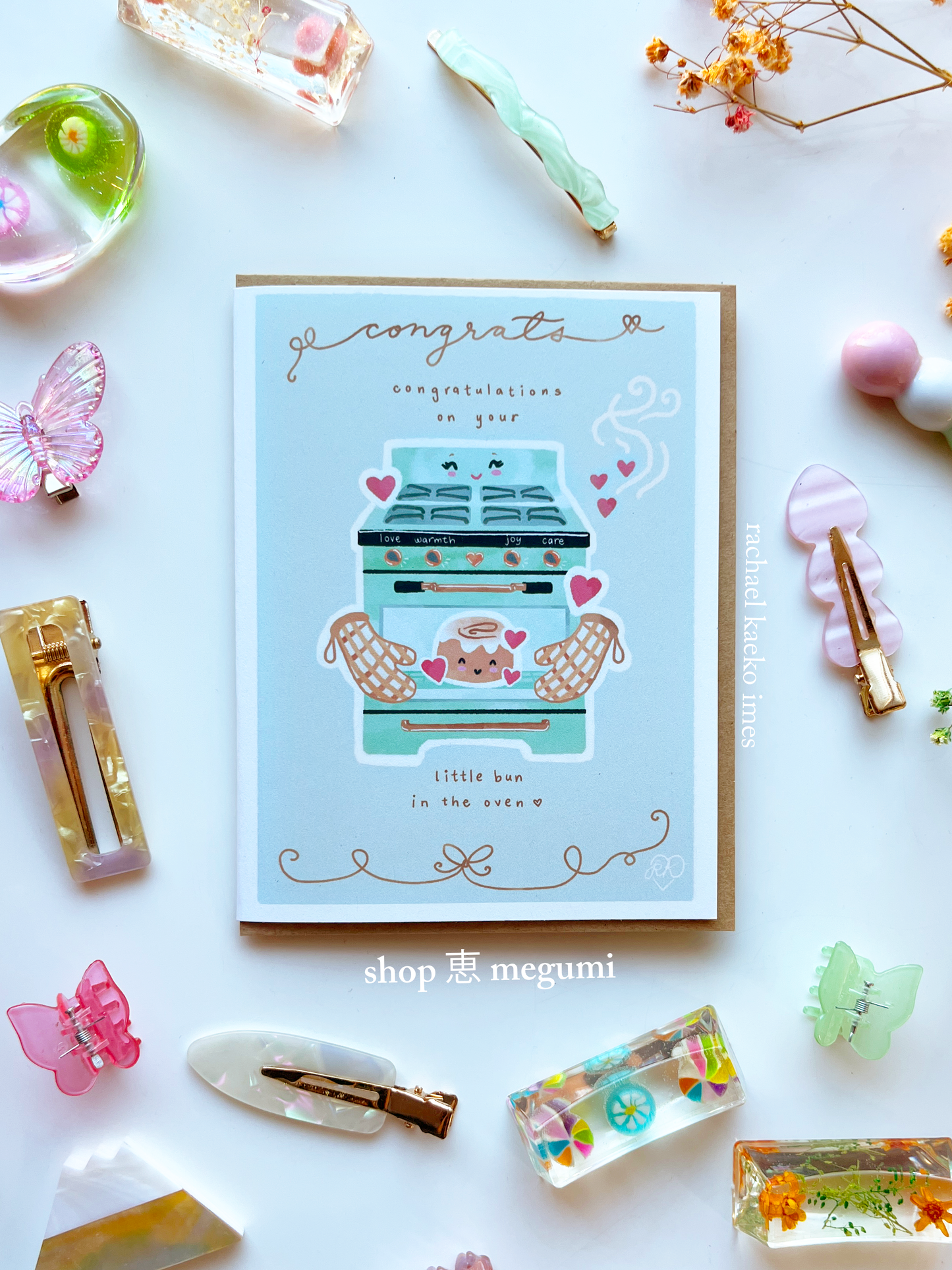 Cute baby shower card with vintage oven and cinnamon bun illustration surrounded by decorative items on a white background