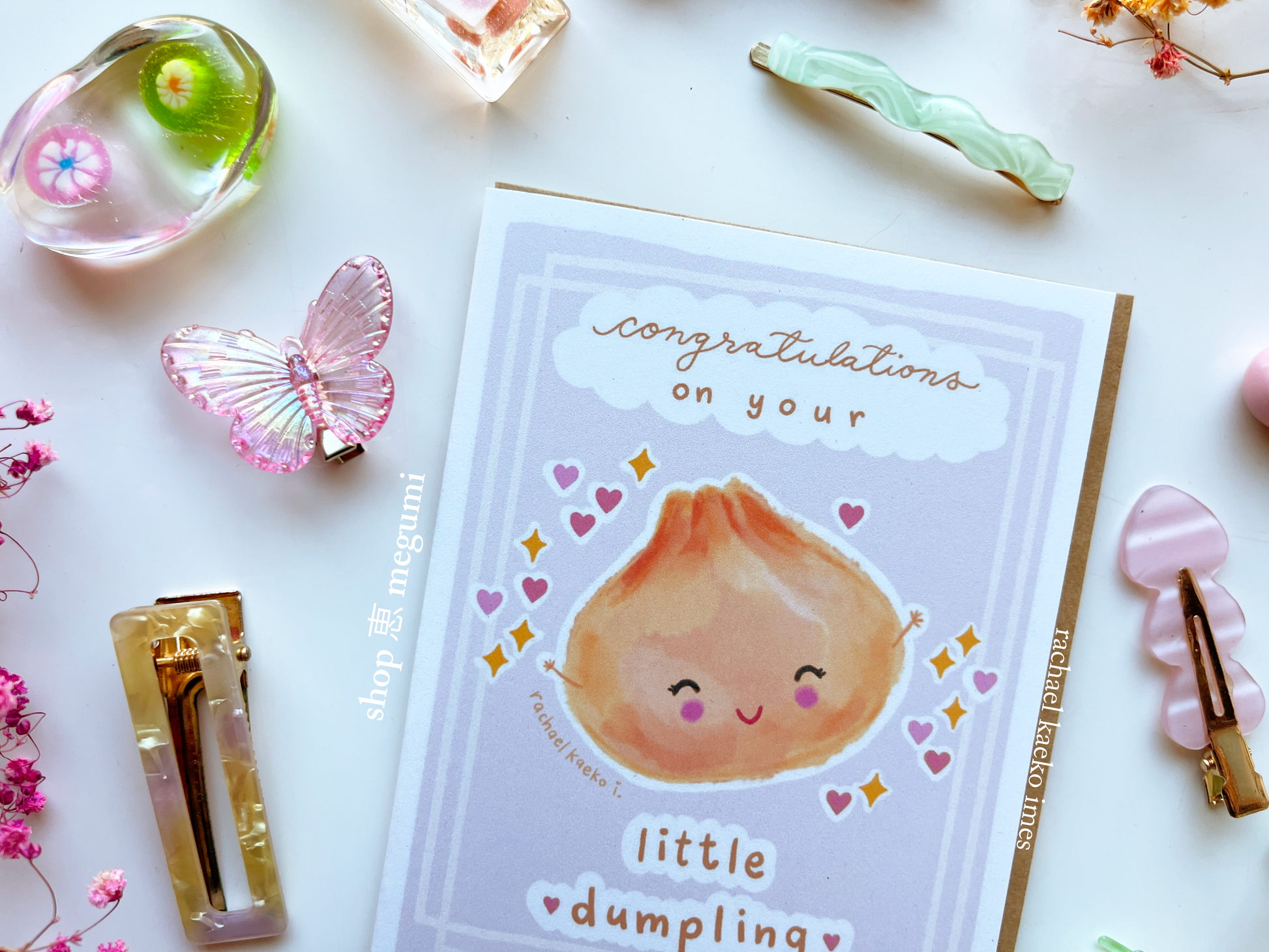 Cute baby shower greeting card with a cute dumpling illustration and text on a decorative background with hair clips and flowers.