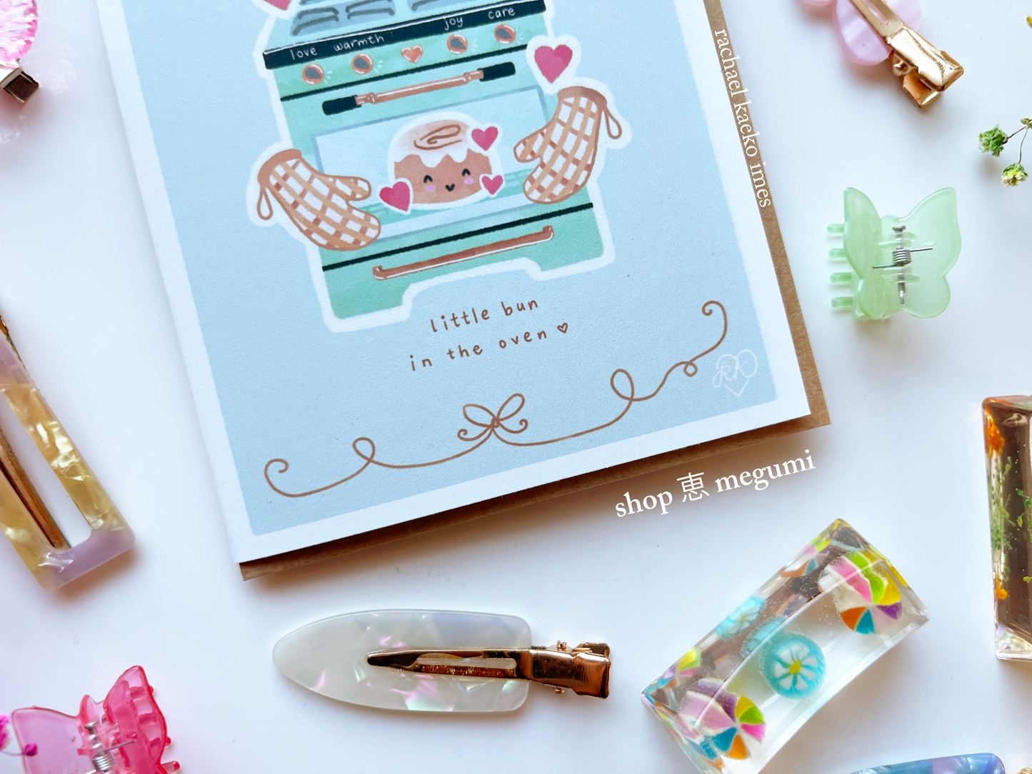 Cute baby shower card with baby little bun in the oven design surrounded by decor on a white surface.