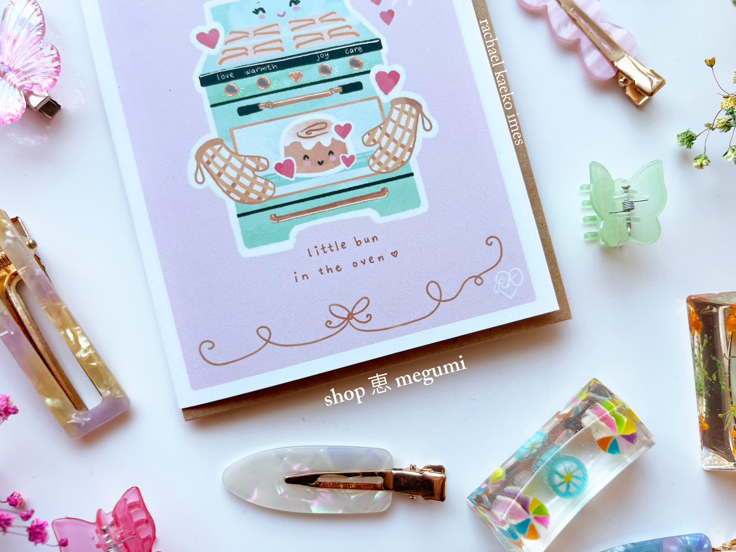 Cute baby shower card with little bun in the oven illustration on a white surface with decorative items