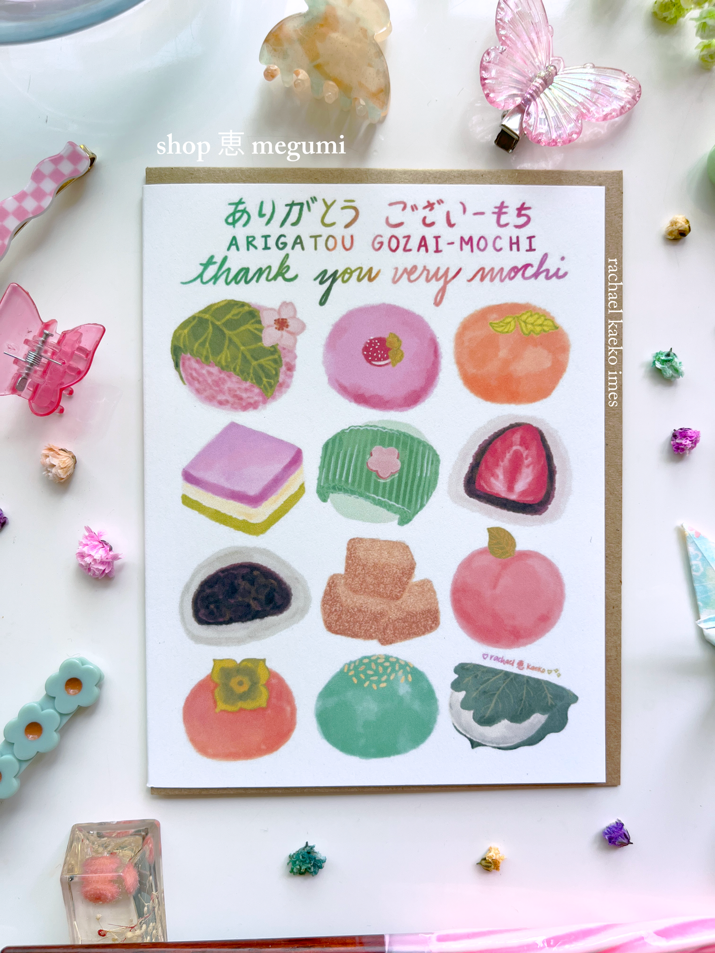 Japanese-inspired greeting card with illustrations of mochi and text that reads 'Arigatou Gozaimochi' and 'Thank You Very Mochi' in English and Japanese on a white background with decorative items.