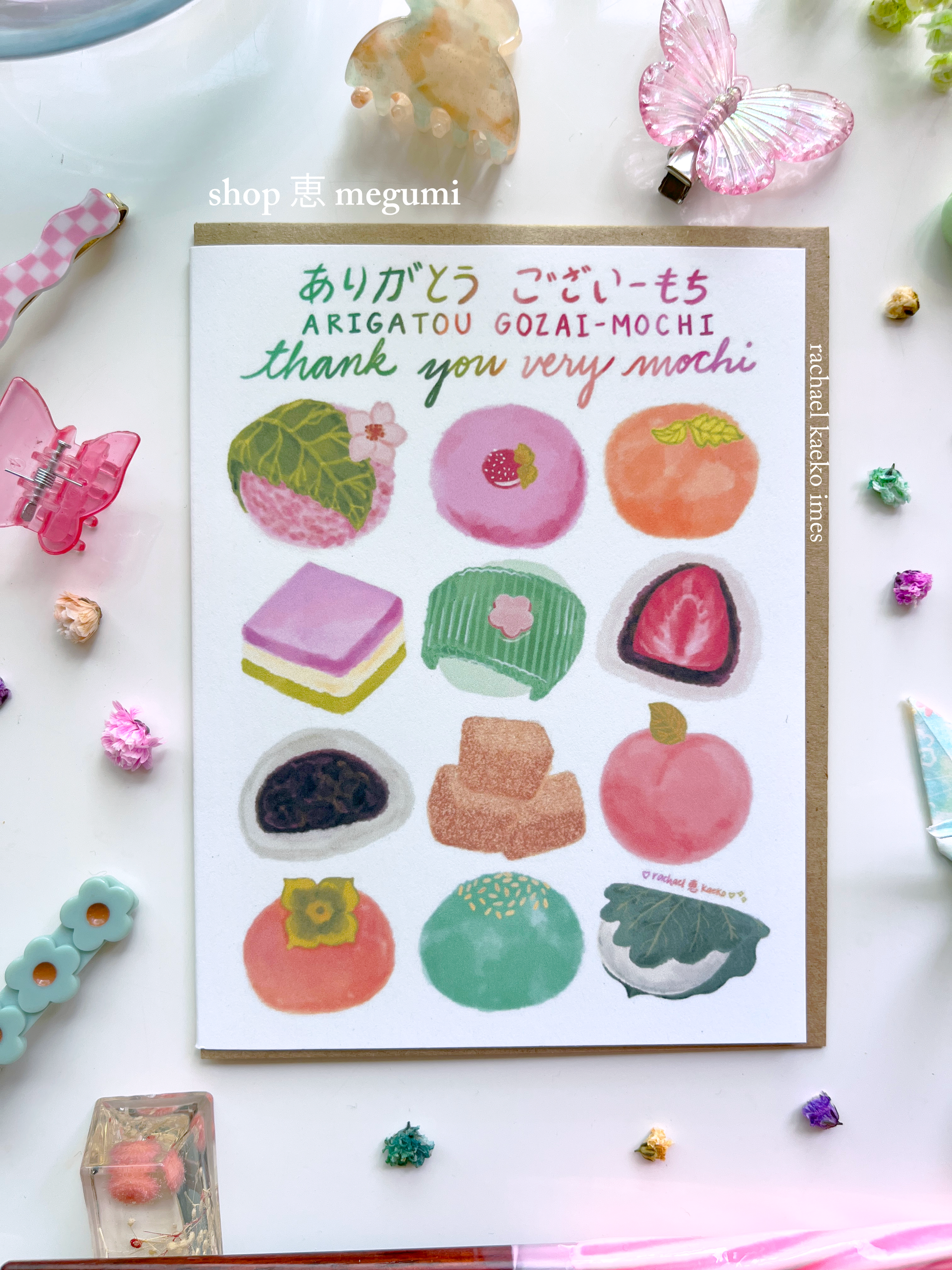 Japanese-inspired greeting card with illustrations of mochi and text that reads 'Arigatou Gozaimochi' and 'Thank You Very Mochi' in English and Japanese on a white background with decorative items.