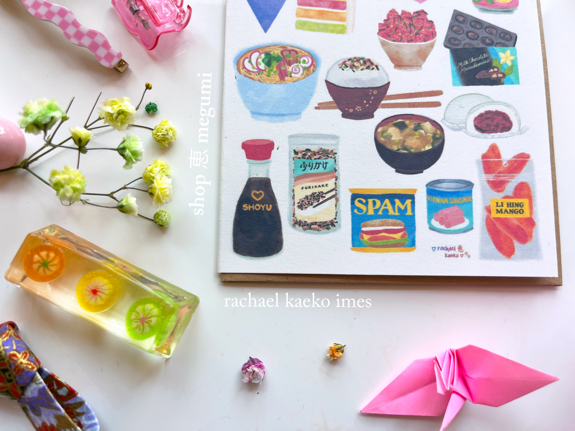 Close-up of Hawaii-inspired greeting card of Hawaii-style food illustrations, on a white surface with colorful items.