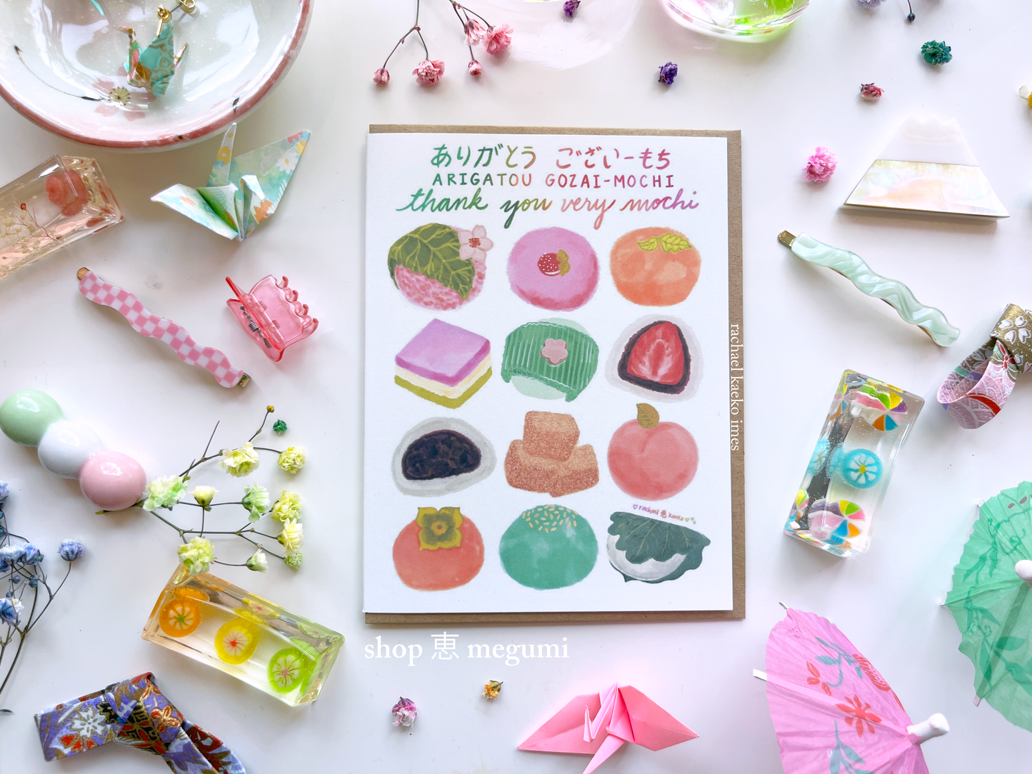 Greeting card with illustrations of mochi and text that reads 'Arigatou Gozaimochi' and 'Thank You Very Mochi' in English and Japanese on a white background with decorative items.