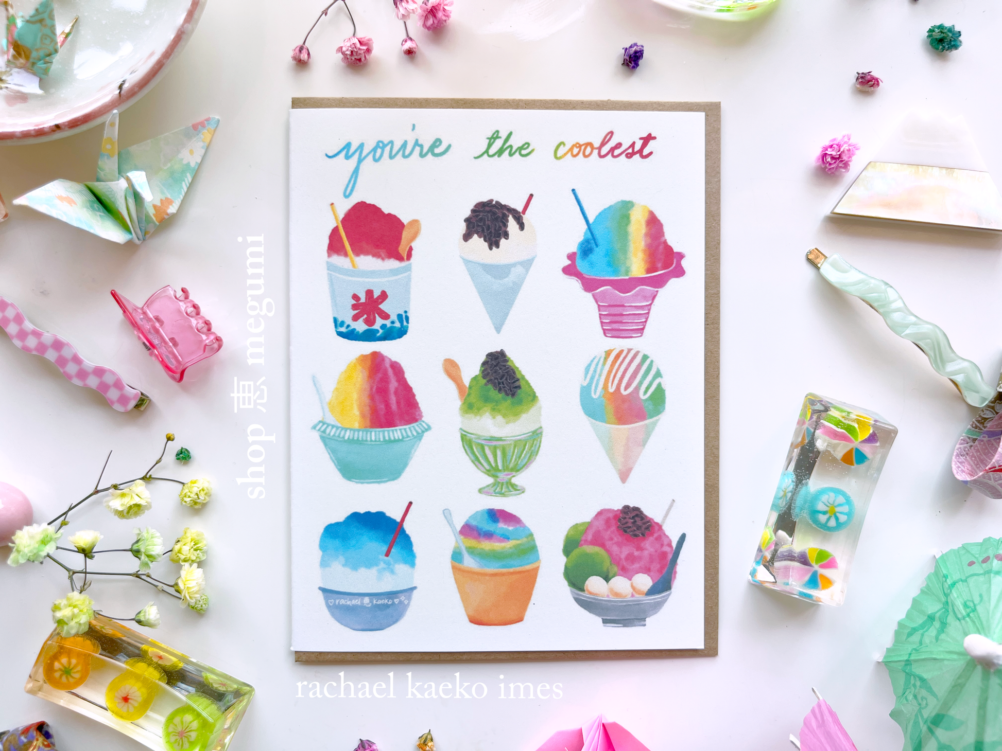 Greeting card with colorful illustrations of Japanese kakigori snow cones and Hawaiian shave ice, and text that reads "You're the Coolest", on a white surface with decorative items.
