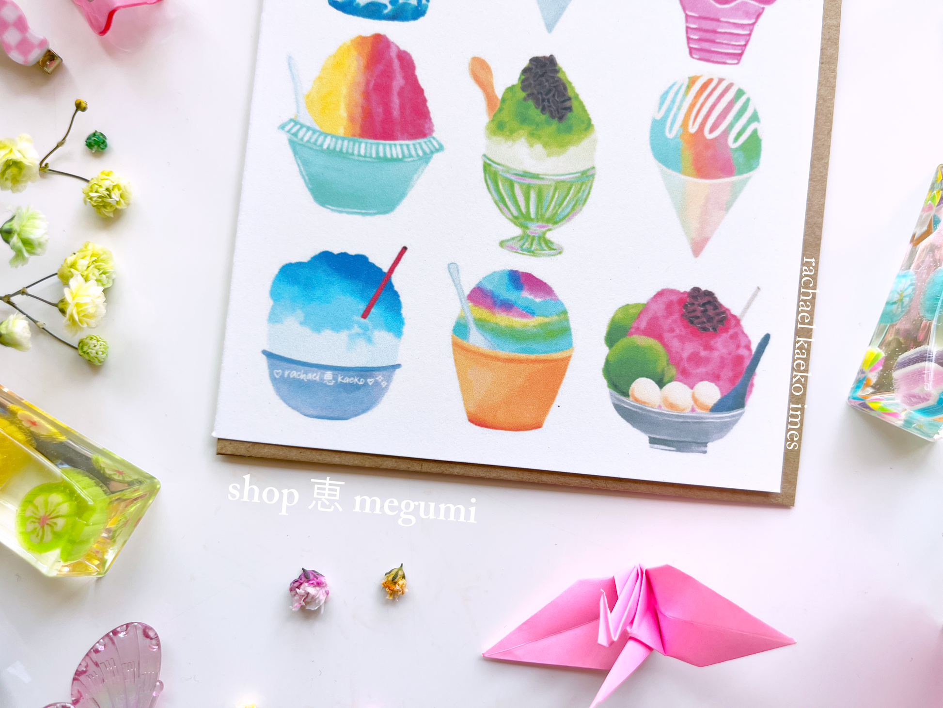 Close-up of greeting card with Japanese snow cone and Hawaiian shave ice illustrations, on a white surface with decorative items.