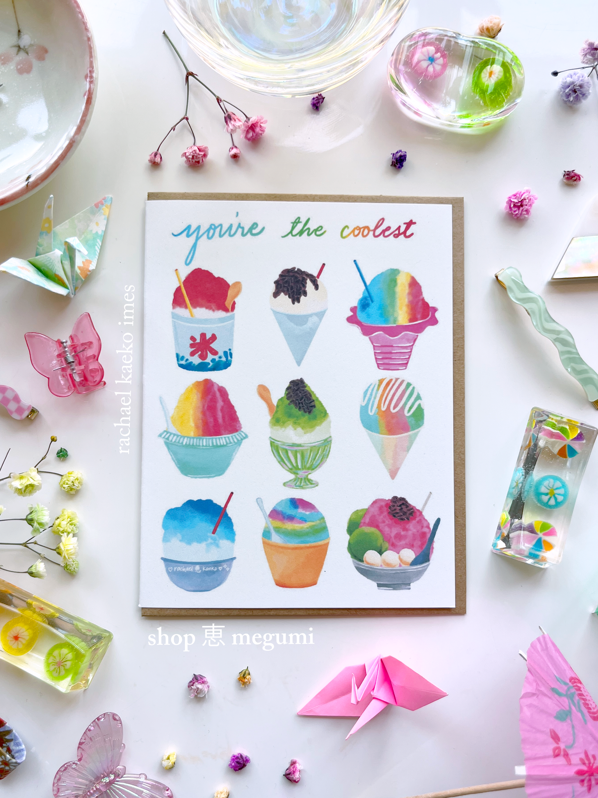 Greeting card with colorful illustrations of Japanese kakigori snow cones and Hawaiian shave ice, and text that reads "You're the Coolest", on a white surface with decorative items.