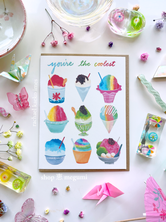 Greeting card with colorful illustrations of Japanese kakigori snow cones and Hawaiian shave ice, and text that reads "You're the Coolest", on a white surface with decorative items.
