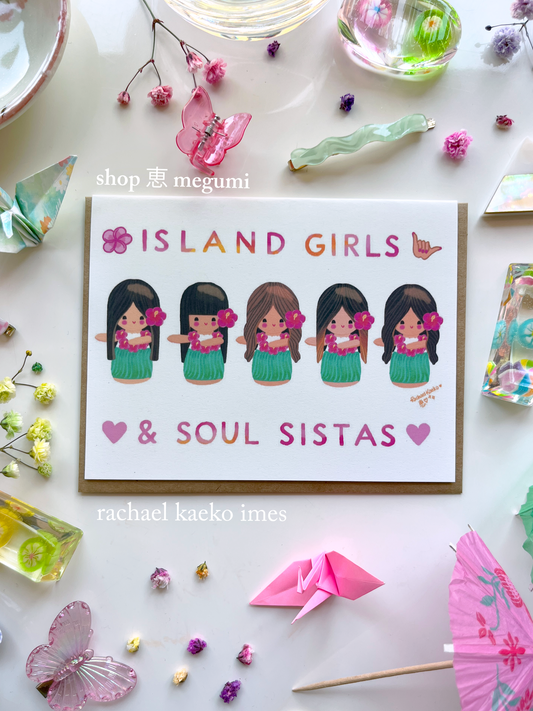 Colorful Hawaii-inspired greeting card featuring original Shop Megumi kokeshi hula girls illustrations, with text that reads "Island Girls & Soul Sistas", on a white surface with decorative items.