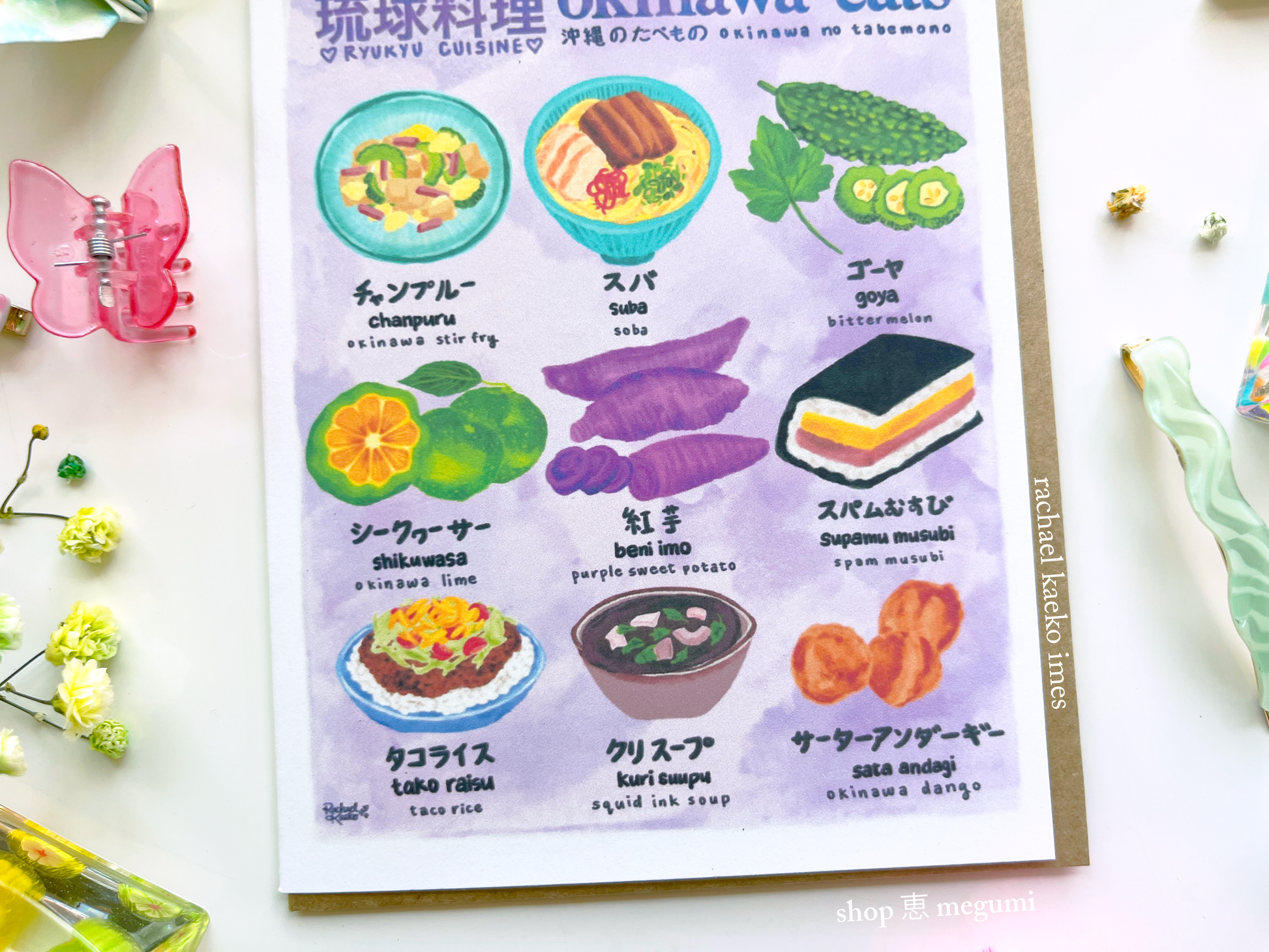 Close up image of "Okinawa Eats" greeting card with illustrations and text about Okinawa cuisine on a white surface with decorative items.