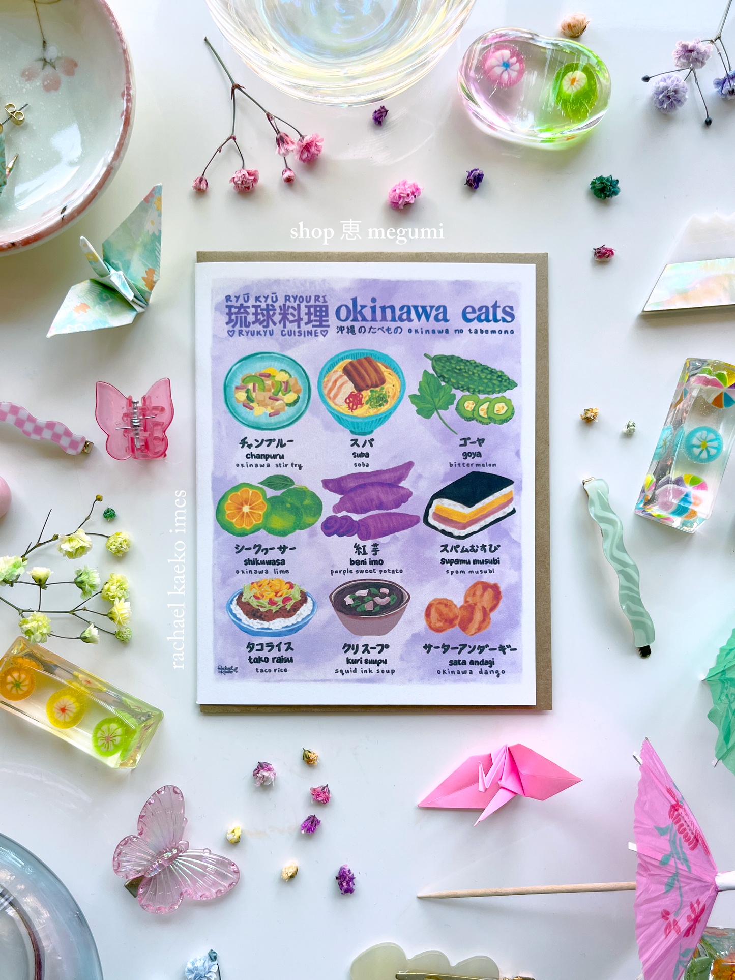 Colorful greeting card titled 'okinawa eats' with illustrations of Okinawan dishes on a decorative background with origami and flowers.