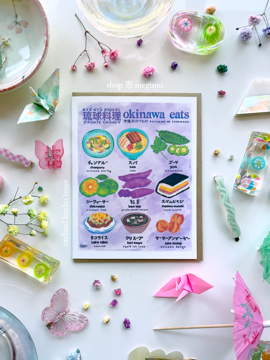 Colorful greeting card titled 'okinawa eats' with illustrations of Okinawan dishes on a decorative background with origami and flowers.
