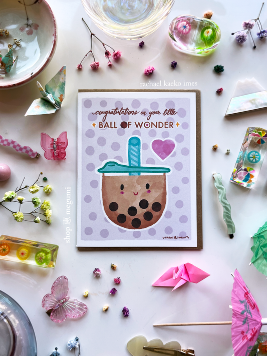 Greeting card with a cute bubble tea illustration surrounded by decorative items on a light surface.